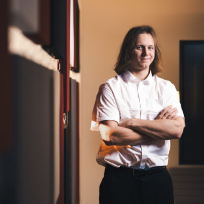 Felix smiling with arms crossed. He wears a white short sleeved shirt with black trousers.