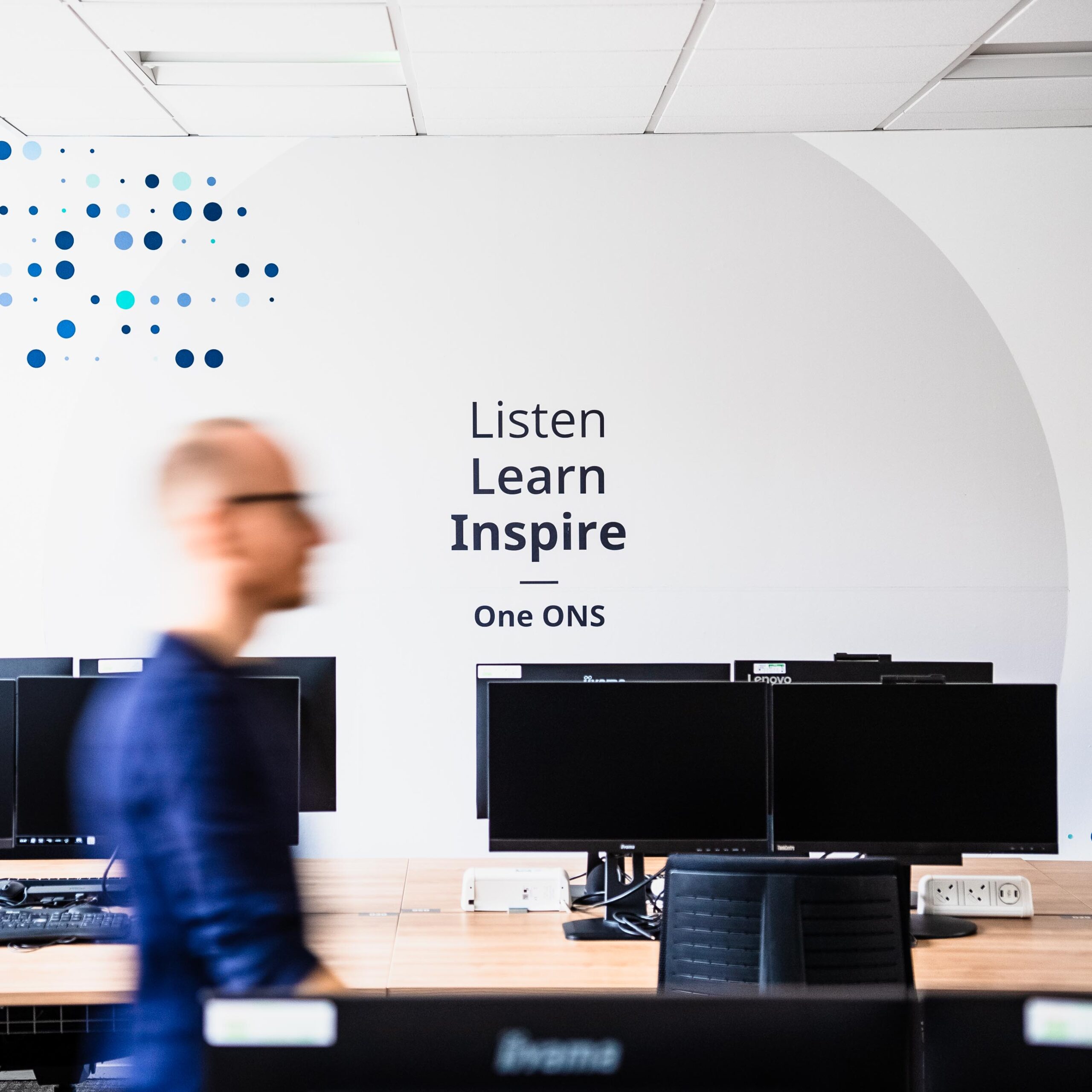 Man walks past a wall mural which reads Listen, Learn, Inspire - Ons ONS.