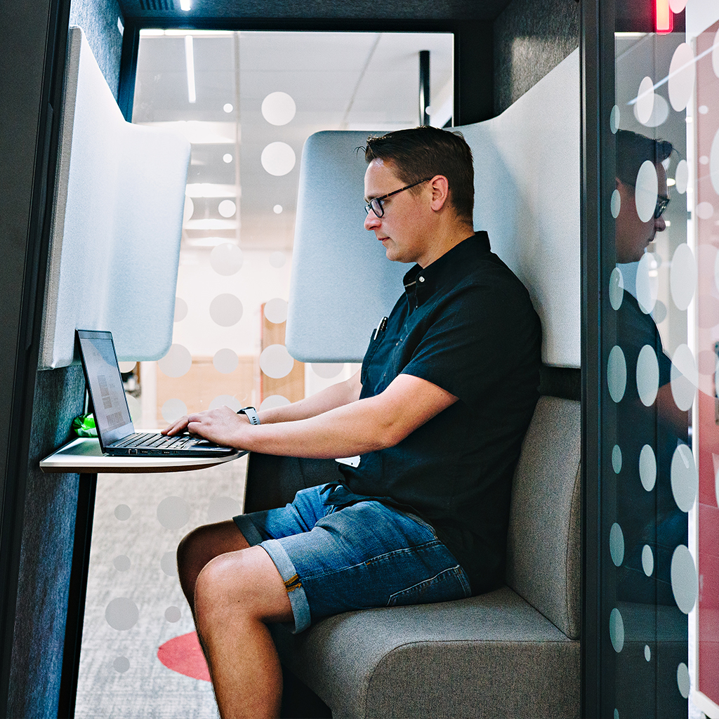 Man focussing alone in a privacy pod, he's working on a laptop.